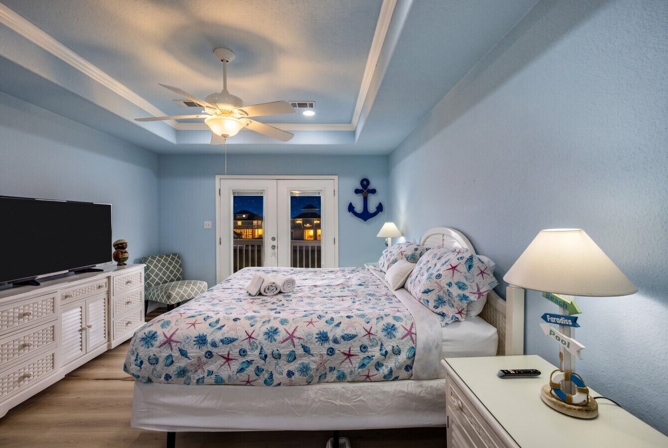 A bedroom with a bed, a television, a ceiling fan, and a nightstand with a lamp.
