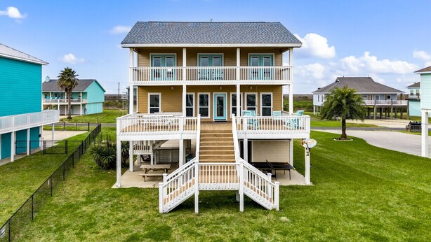 A two-story building with a central staircase, multiple balconies, and a surrounding grassy area. - Classic Coastal Beach Home Perfect for Families (Crystal Beach)