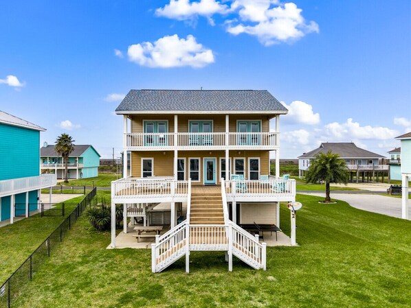 A two-story building with a central staircase, multiple balconies, and a surrounding grassy area.