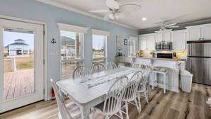 A modern kitchen with white cabinetry, a stainless steel refrigerator, and a dining area with white chairs and a table. - Classic Coastal Beach Home Perfect for Families (Crystal Beach)