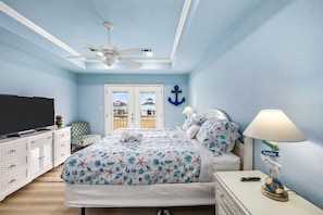 Un dormitorio con cama, televisor, ventilador de techo y lámpara.