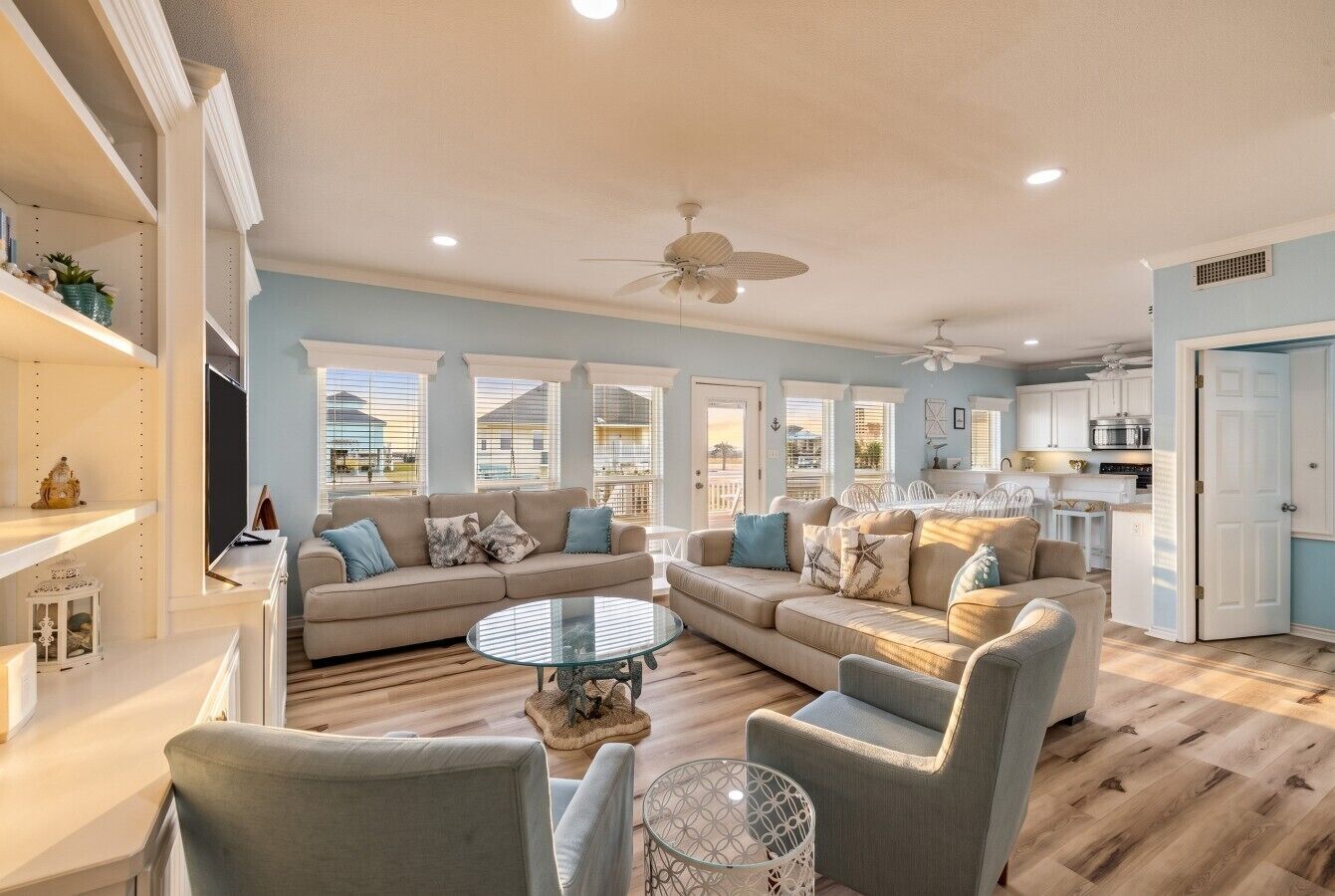 A spacious living room with a large sofa set, a glass coffee table, and a dining area with a white table and chairs.