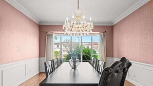 Comedor con una mesa grande, sillas, una lámpara de araña y vistas al exterior.