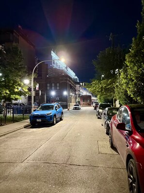 Ein beleuchtetes Straßenszenario bei Nacht mit parkenden Autos und einem Gebäude mit leuchtenden Schildern.