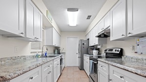 Eine moderne Küche mit weißen Schränken, Granit Arbeitsplatten, einem Edelstahlk ühlschrank und einem schwarzen Backofen.