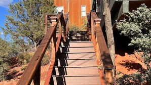 Eine Holztreppe führt zu einem Gebäude mit rotem Dach, umgeben von Bäumen und Sträuchern.
