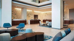 Eine geräumige Lobby mit Empfangstresen, Sitzbereichen und einer hohen Decke mit strukturierter Wand.