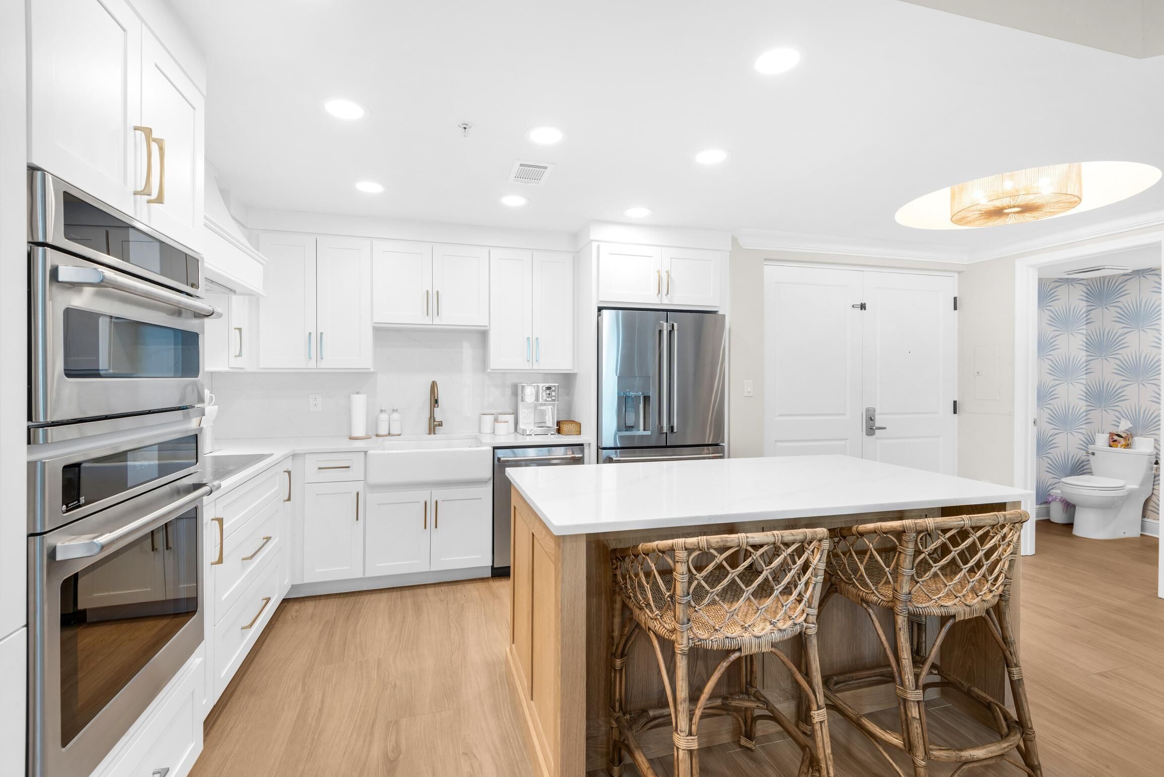 A modern kitchen with white cabinetry, stainless steel appliances, and a central island with wicker barstools.