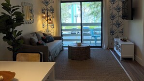 Un salon moderne comprenant un canapé, une table à manger, une grande fenêtre offrant une belle vue et un téléviseur à écran plat fixé au mur.