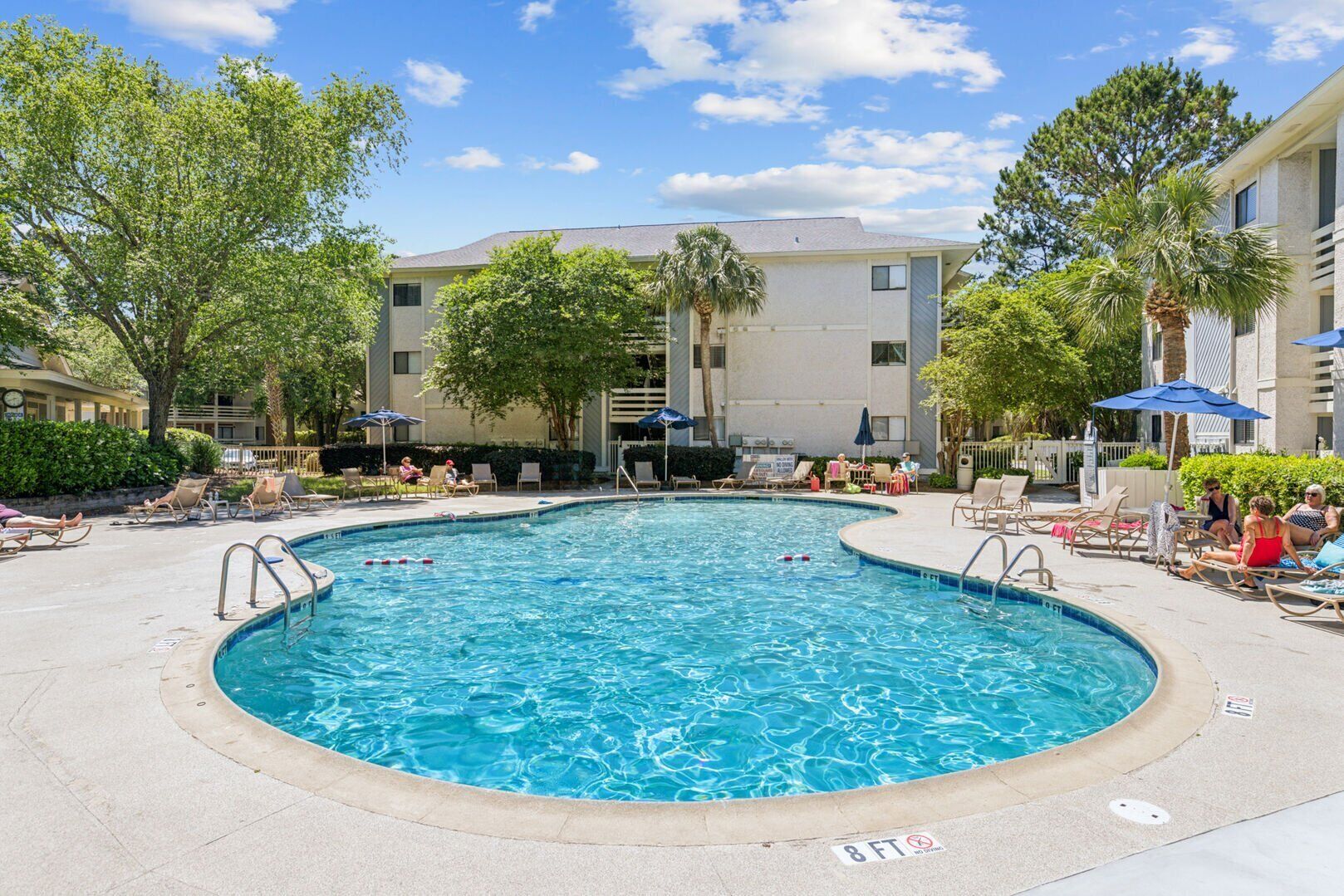 A swimming pool surrounded by lounge chairs and umbrellas, with a building in the background.