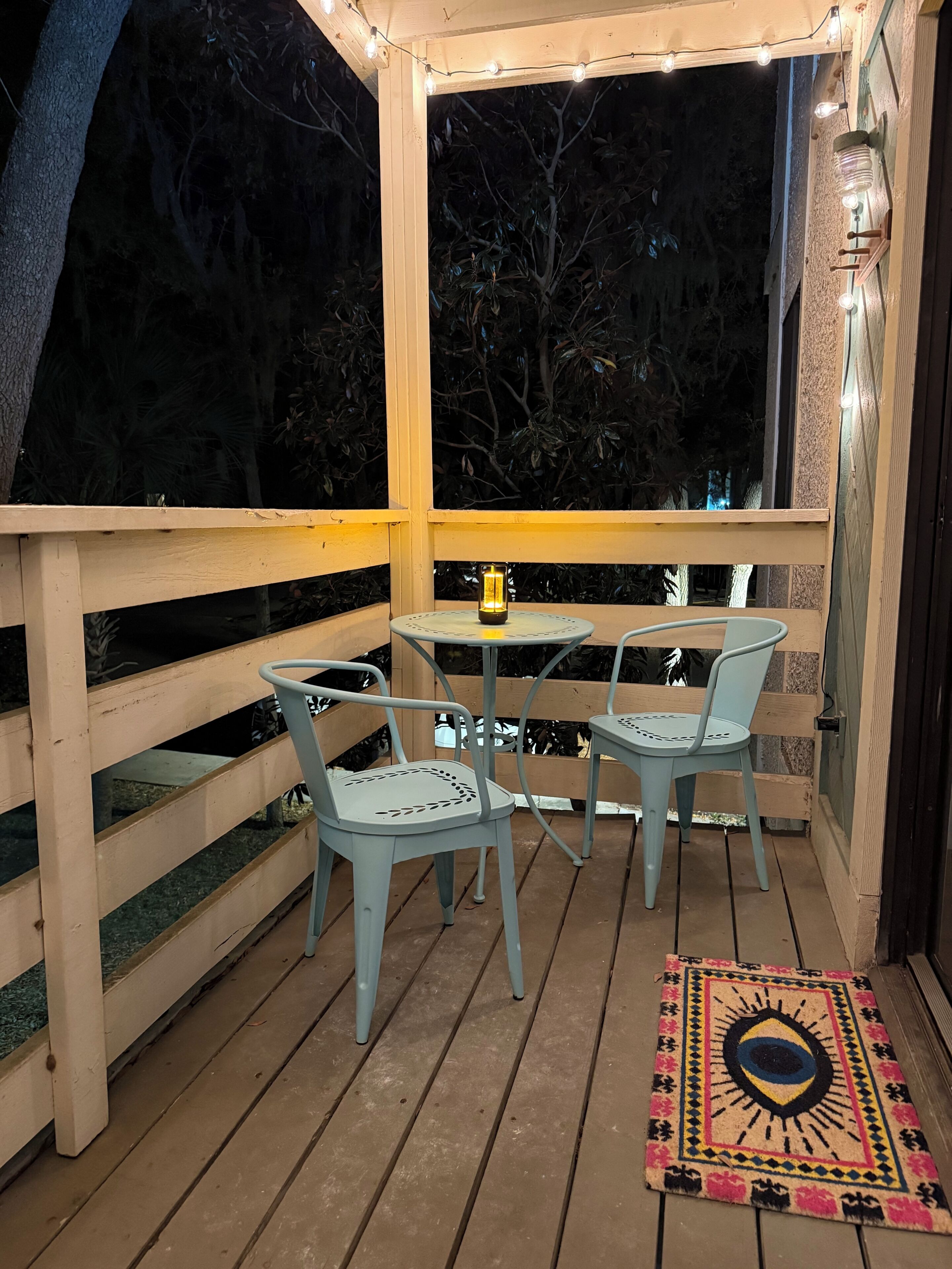 Une terrasse en bois avec deux tables et des chaises, un tapis décoratif et des guirlandes lumineuses.