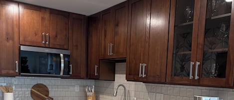 Une cuisine moderne avec des meubles en bois, un four à micro-ondes en acier inoxydable, un lave-vaisselle et un plan de travail blanc.