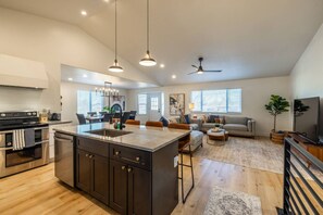 A spacious living area with a kitchen, dining space, and a seating area with a sofa and coffee table. - Meeting Place | Hot Tub, Theater Room, Mini Golf, Foosball (Sandy)