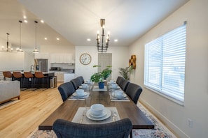 A modern kitchen with white cabinets, a stainless steel refrigerator, and a dining area with a wooden table set for six.
