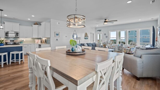 A spacious kitchen with white cabinetry, a wooden dining table, and a ceiling fan. - Ocean Views with Heated Pool! One Row from Beach! (Oak Island)