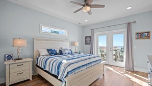 A bedroom with a bed, nightstands, a ceiling fan, and a view to the outside. - Ocean Views with Heated Pool! One Row from Beach! (Oak Island)