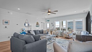 A spacious living room with a grey sofa set, a coffee table, and a ceiling fan. - Ocean Views with Heated Pool! One Row from Beach! (Oak Island)