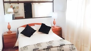 Une chambre bien rangée, avec un lit, des tables de chevet, un miroir et une fenêtre avec des rideaux.
