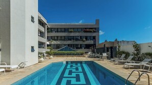 Une piscine dont le fond est décoré de motifs géométriques en mosaïque, entourée de chaises longues et de plantes en pot, avec un immeuble à plusieurs étages en arrière-plan.