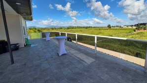 Une terrasse avec deux tables blanches et une balustrade donnant sur un paysage verdoyant.