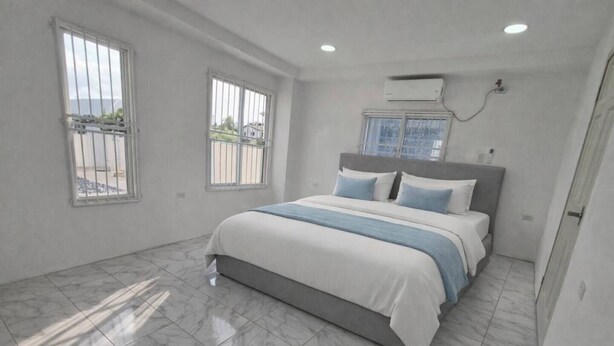 Une chambre à coucher avec un lit, deux fenêtres, un appareil de climatisation et un sol carrelé.