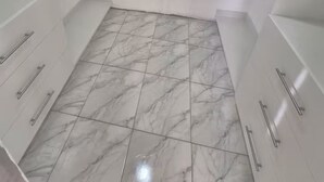 Une salle de bain avec des meubles blancs, un sol carrelé et un espace douche.