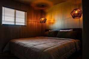 Ein Schlafzimmer mit einem großen Bett, einem Fenster mit Jalousien und zwei Hängeleuchten.