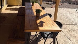 Een buitenpatio met een houten tafel en banken, een barbecue en een plafondventilator.