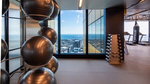Un gimnasio con equipo de ejercicio, amplias ventanas con vista a la ciudad y un techo alto.