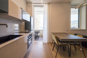 A modern kitchen with a dining area, a view through a doorway, and a window with a view of the city.