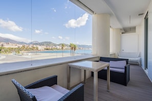 A balcony with wicker furniture, a small table, and a view of a coastal cityscape.