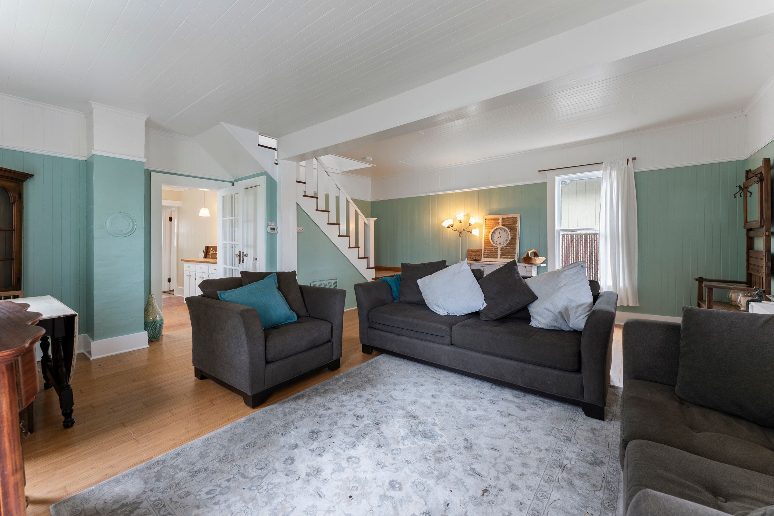 A spacious living room with two grey sofas, a patterned rug, and a staircase leading to another room.
