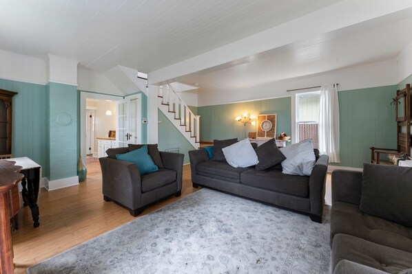 A spacious living room with two grey sofas, a patterned rug, and a staircase leading to another room.