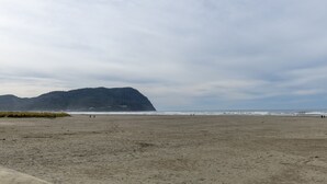En bred sandstrand med utsikt över ett avlägset berg och havet.