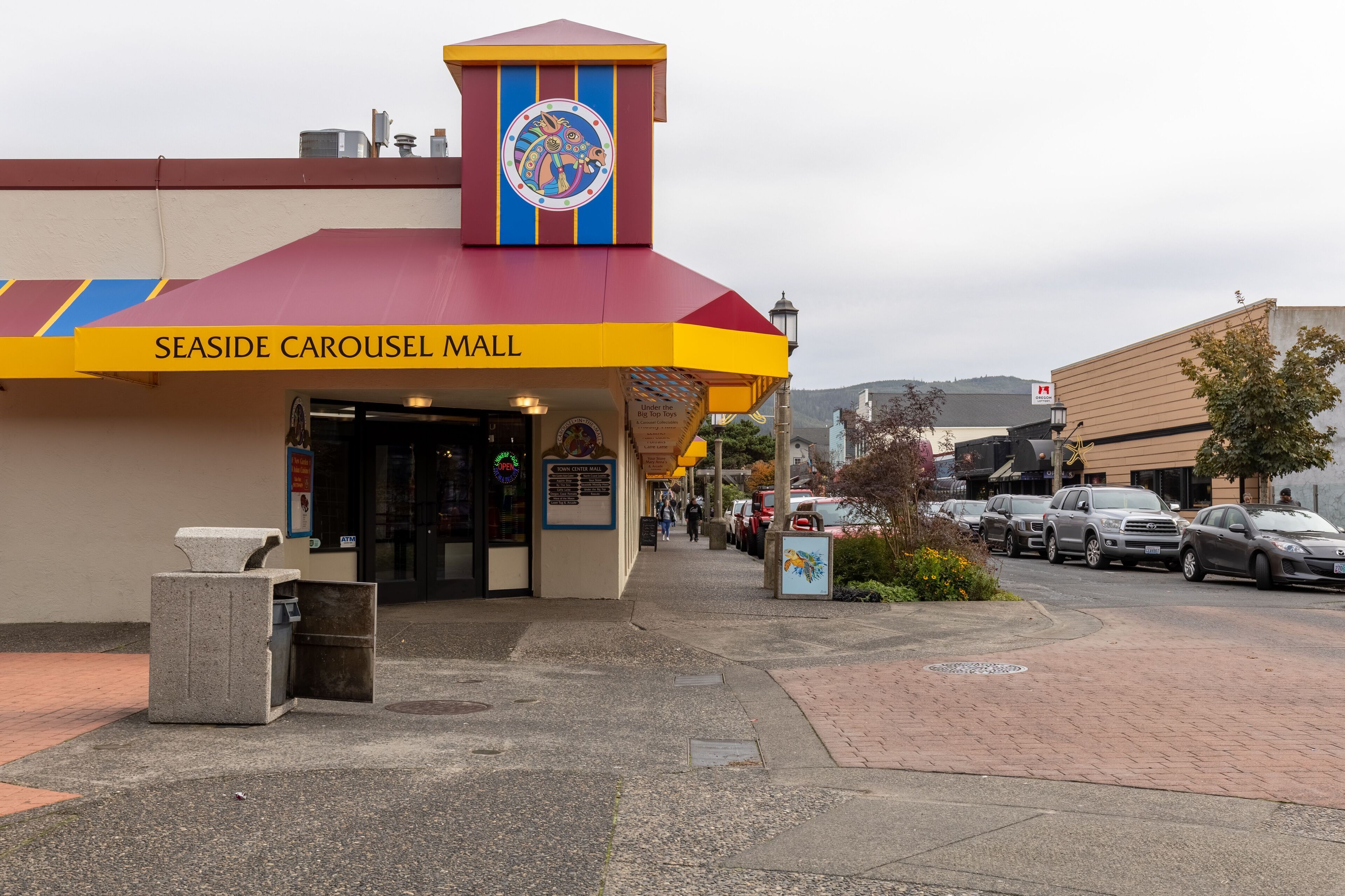 Das Außengelände des Seaside Carousel Mall mit einem markanten Eingang, einem Mülleimer und parkenden Autos.