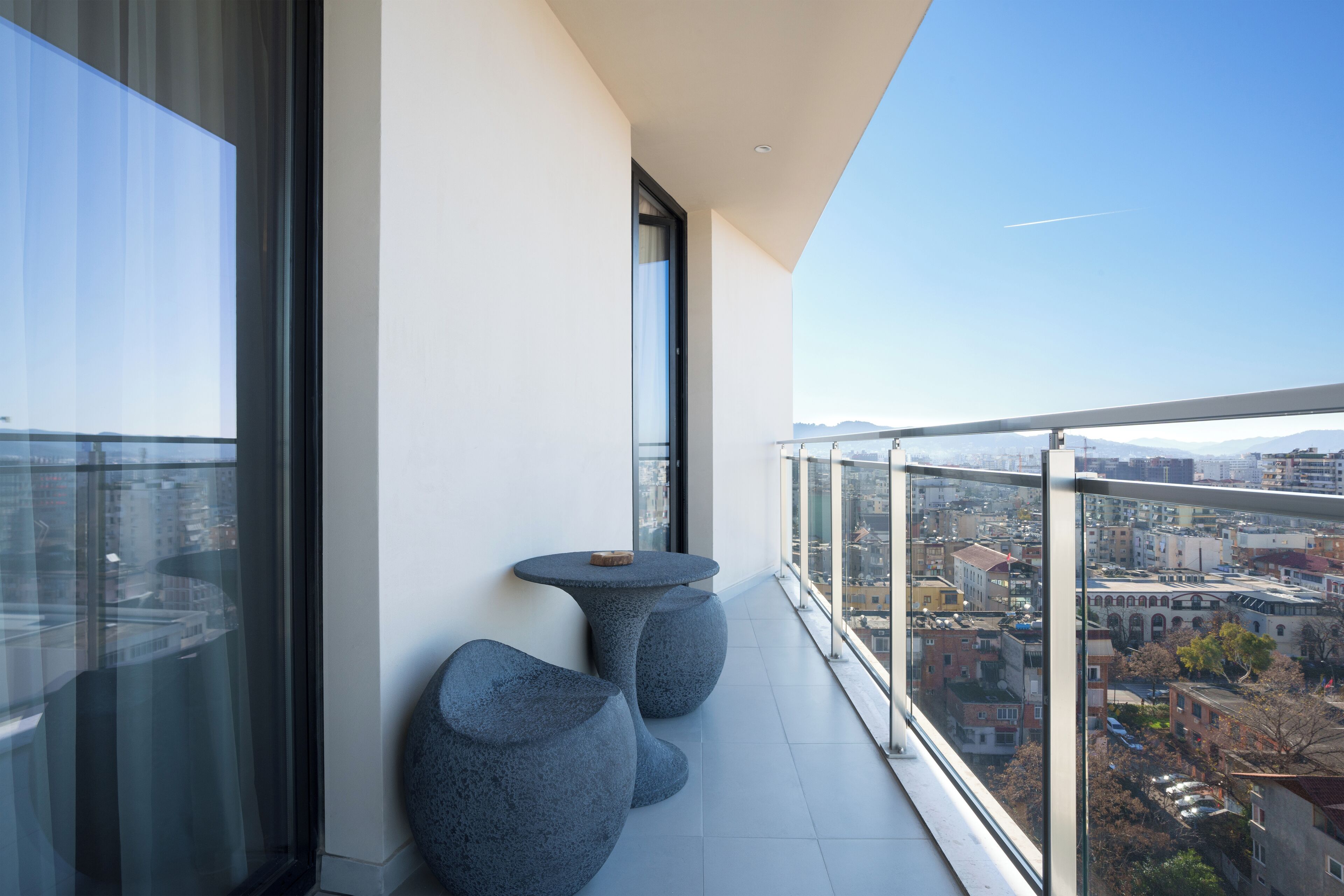 A balcony with a glass railing, two round tables, and a view of the cityscape.