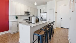 A modern kitchen with white cabinets, stainless steel appliances, and a central island with bar stools. - Carolina Horizon - Pool, City Views, Free Parking (Charlotte)