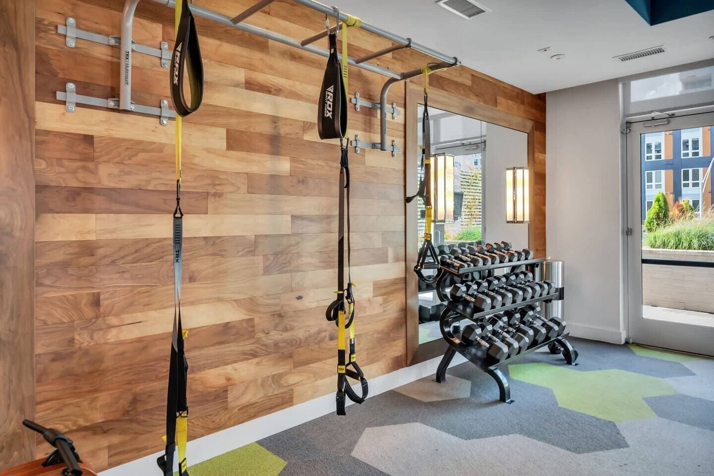 Een sportschool met TRX-schorsingsbanden, een rek met gewichten en een houten wand.