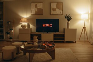 Un saló amb televisió que mostra 'NETFLIX', una làmpada, un vas amb plantes i una estanteria.