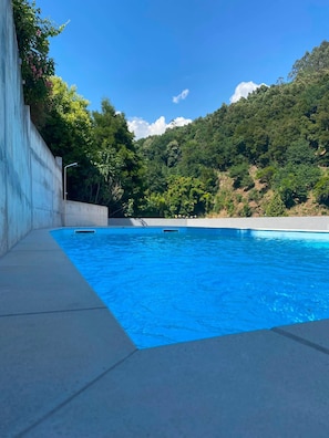 A swimming pool with a concrete deck, surrounded by lush greenery and a hilly landscape. - Gerês Thermae Retreat | Luxury Apartment & Pool (Terras de Bouro)