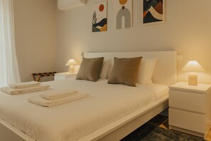 Et hotelværelse med en seng, to sengeborde, en kommode og en væg med abstrakt kunst.