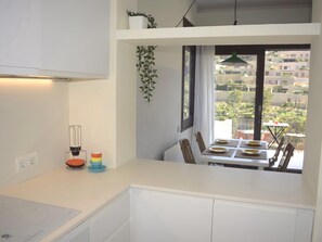 A modern kitchen with a dining area, a balcony with a view, and a hanging plant. - Apartament Brisa Blanca (Begur, Sa Riera) (Begur)