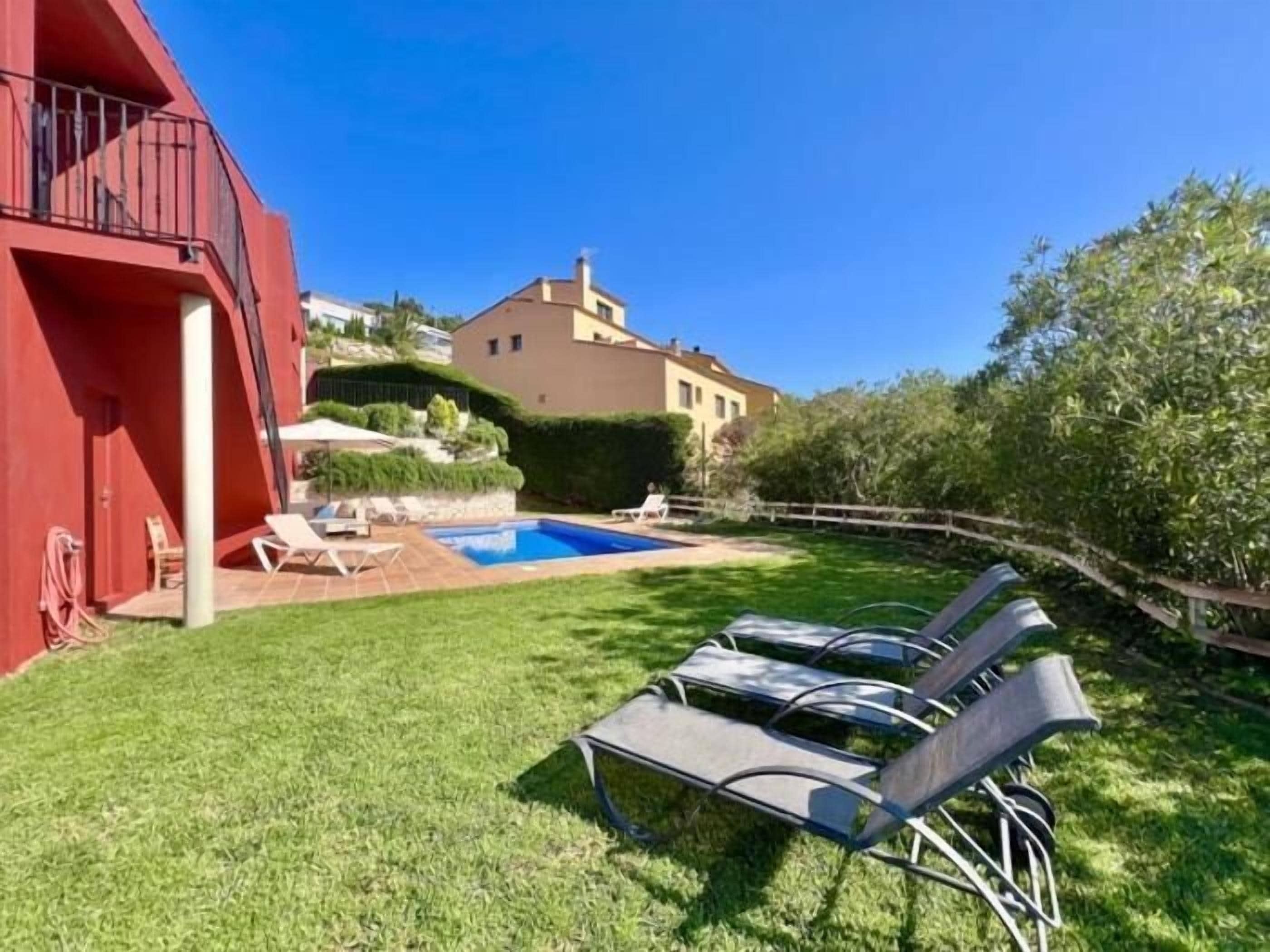 Un giardino con piscina, poltrone relax e un edificio rosso.