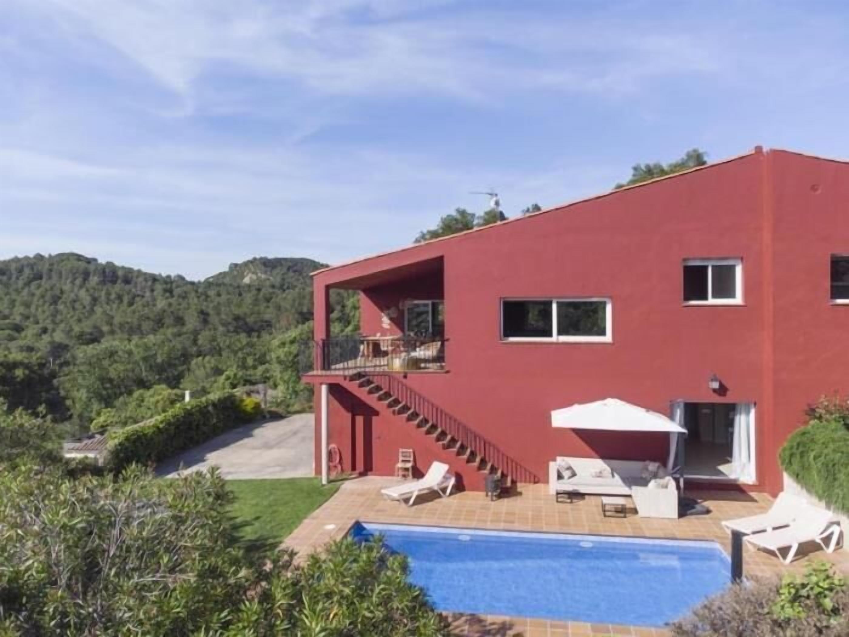 A red two-story building with a pool, outdoor seating, and a staircase leading to a balcony.
