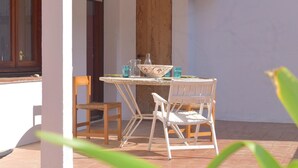A patio with a table and chairs, a wooden door, and a window. - Casa Muga (Tamariu) (Tamariu)