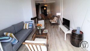 A living room with a grey sofa, a coffee table with a vase of flowers, and a television on a stand. - Gîte de Font Bénite 2 - SAINT-ANDRÉ-LA-CÔTE (SAINT-ANDRÉ-LA-CÔTE)