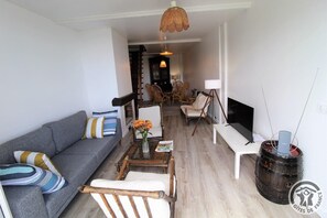 A living room with a grey sofa, a coffee table with a vase of flowers, and a television on a stand. - Gîte de Font Bénite 2 - SAINT-ANDRÉ-LA-CÔTE (SAINT-ANDRÉ-LA-CÔTE)