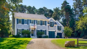 Une maison à deux étages avec un porche à l’avant, une allée et un grand rocher dans le jardin.