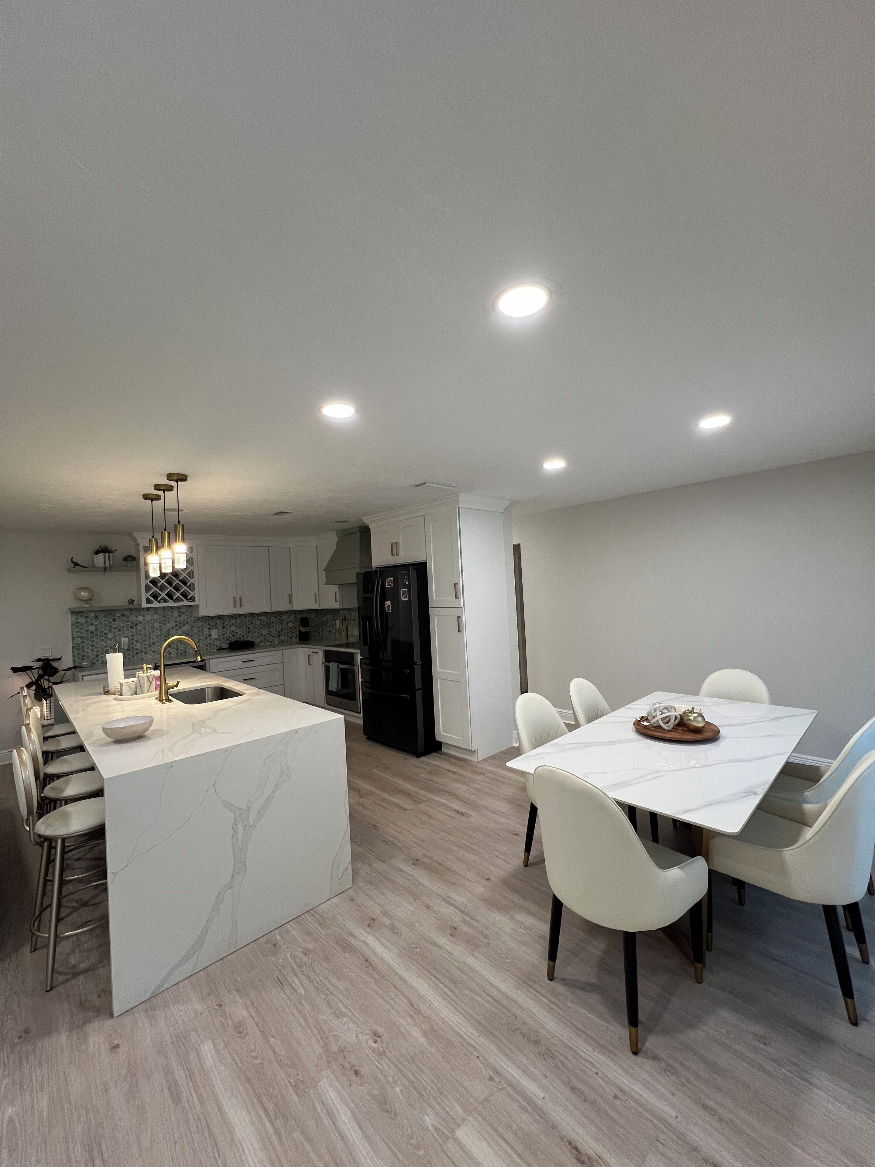 Una cocina moderna con una isla central, armarios blancos y un comedor con una mesa y sillas de mármol.