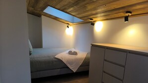 Ein gemütliches Schlafzimmer mit Oberlicht, einem Bett mit gerolltem Handtuch und einer kleinen Küchenzeile.
